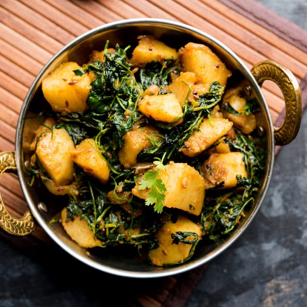 Indian Wok's Aloo Methi, a dish of golden potatoes and green fenugreek leaves, served in a brass bowl.
