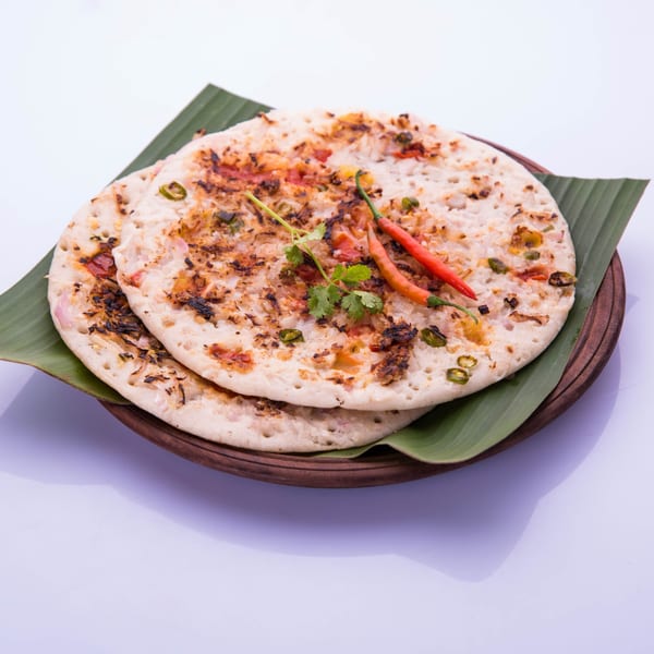 Two Indian Wok uttapams topped with vegetables, cilantro, and red chilies on banana leaves.