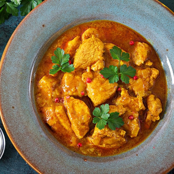 Indian Wok's chicken curry, garnished with fresh parsley and red peppercorns, in a blue bowl.