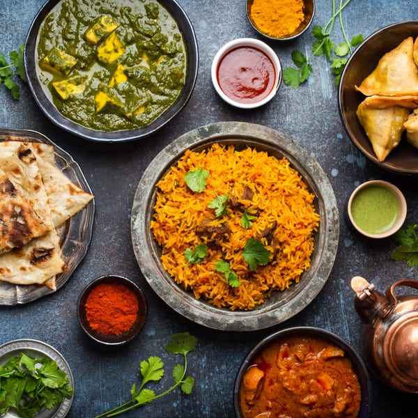 Overhead view of various Indian dishes including palak paneer, biryani, naan, samosas, and curries.