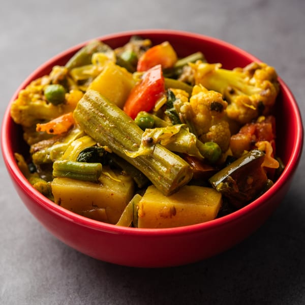 Close-up of a vibrant Indian mixed vegetable curry in a red bowl.
